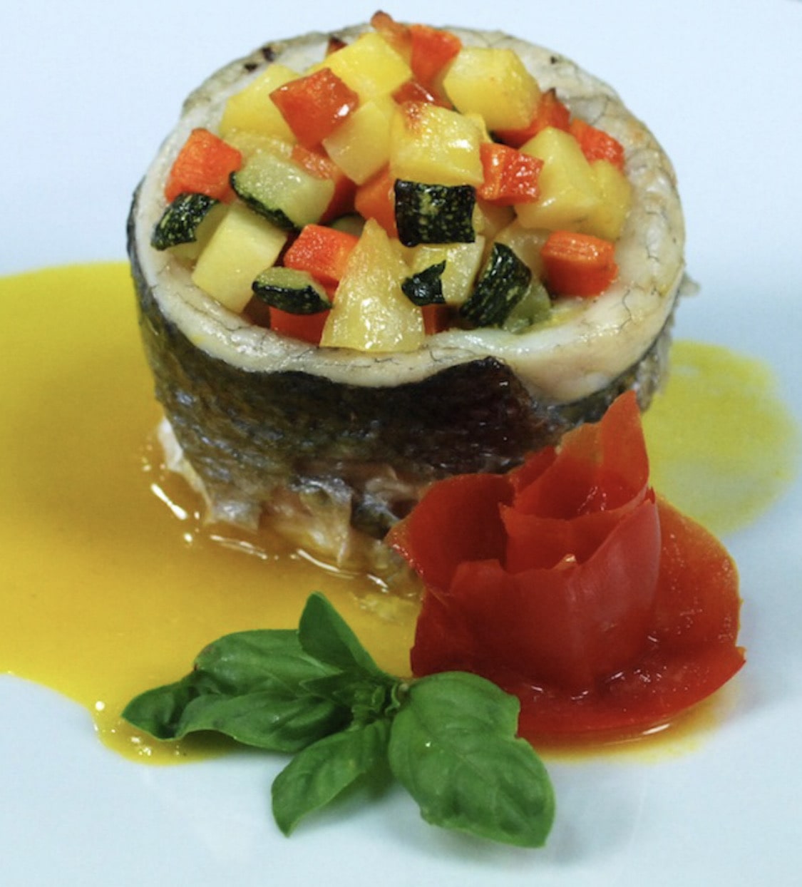 Plated dish featuring a layered cylindrical portion topped with diced vegetables, surrounded by sauce and garnishes.