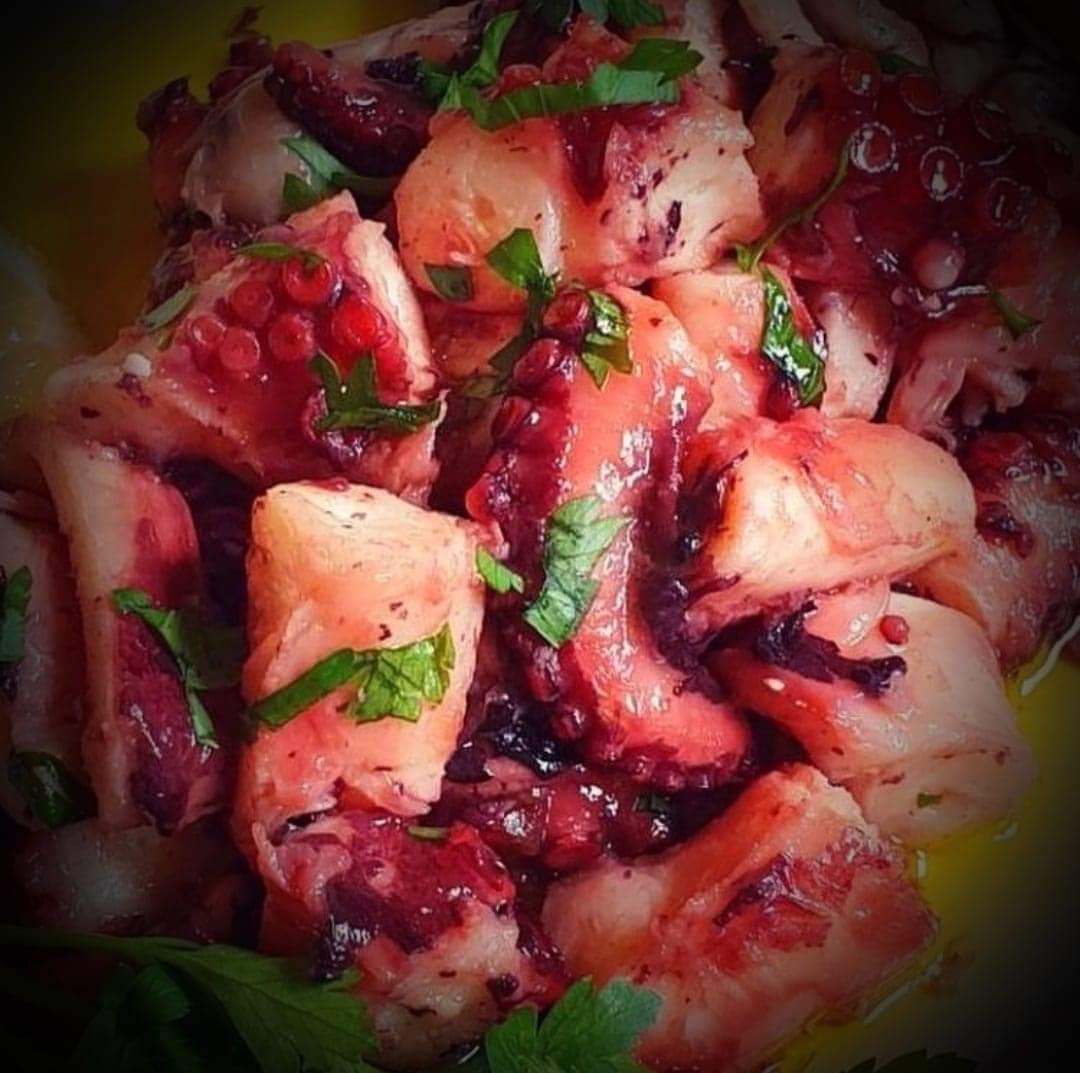 Close-up of chopped octopus pieces garnished with herbs, with dark vignetted lighting.
