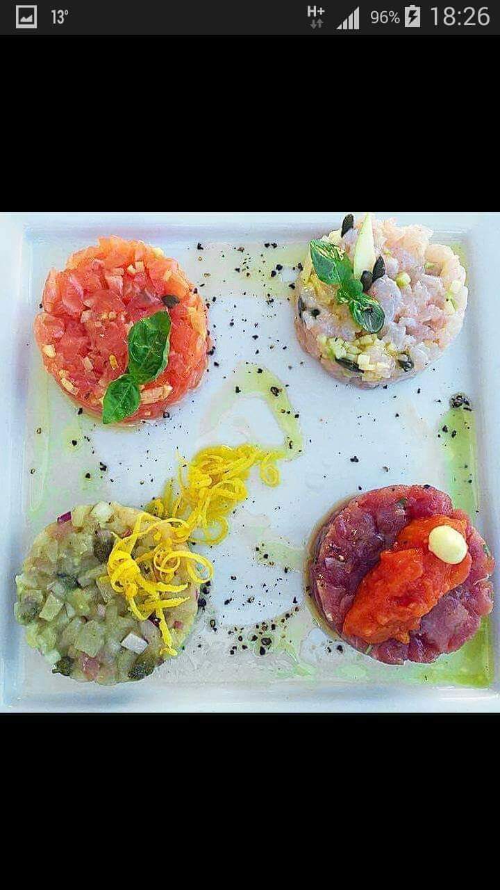 Close-up of four colorful plated seafood preparations arranged on a rectangular white plate, brightly lit.